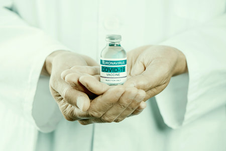 a caucasian healthcare worker man, wearing a white lab coat, has a simulated bottle of covid-19...