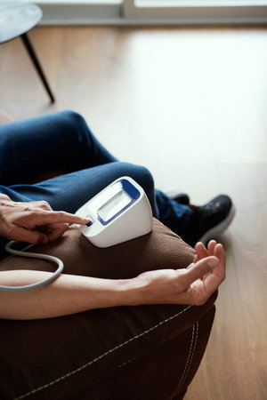 closeup of a caucasian man measuring his blood pressure with an electronic sphygmomanometer, sitting...