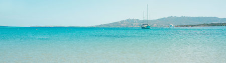 a sailboat and a yacht are sailing on the calm water of the Mediterranean sea in Sardinia, Italy,...