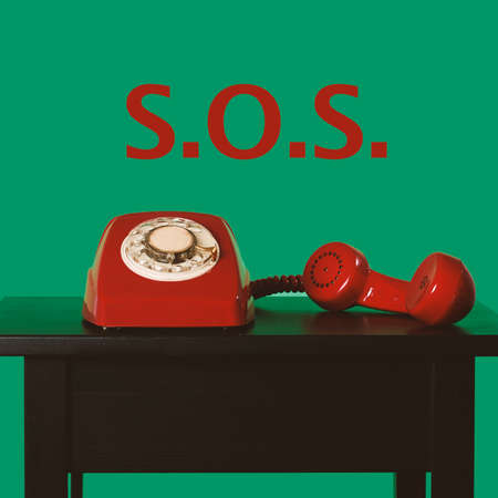 closeup of a red landline rotary dial telephone off-the-hook on a table and text SOS against a green backgroundの写真素材