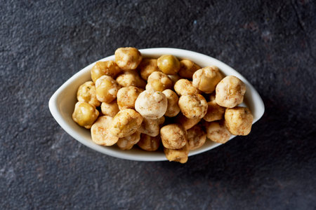 high angle view of some crispy roasted peas in a white ceramic bowl, on a dark gray stone surfaceの写真素材