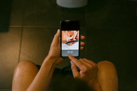 a young caucasian man, sitting in the toilet, dates online in his smartphone, with a simulated app with the word match in its screenの写真素材