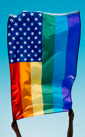 someone waves a rainbow US flag on the blue skyの写真素材