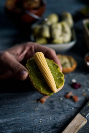 closeup of a young caucasian man having a vegan sandwich, made with guacamole and baby sweetcorn, in...