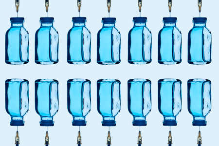 some vaccine bottles, with a blue liquid inside, and some syringes stuck on them, arranged in different lines on a pale blue backgroundの写真素材