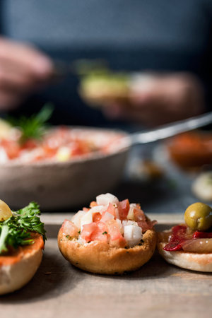 closeup of some vegan sandwiches, with different toppings, to eat as snacks or appetizers, placed on a gray table and a man preparing some more in the backgroundの写真素材