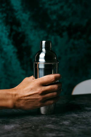 closeup of a young caucasian man grabbing a metal cocktail shaker from a dark table or countertopの写真素材