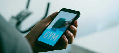 a young caucasian man is looking to his smartphone, that reads gym in its screen, next to a...