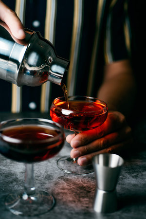 closeup of a young caucasian man, wearing a striped shirt, saerving a cocktail, from a metal shaker,...