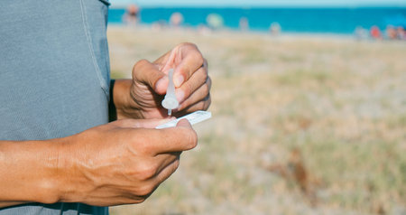 closeup of a young caucasian man on the beach, in casual wear, placing his own sample into the...
