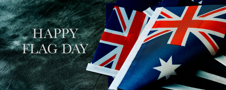 closeup of some australian flags and the text happy australia day on a dark gray background, in a panoramic format to use as web banner or headerの写真素材