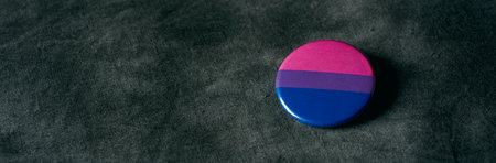 a badge patterned with a bisexual pride flag, on a dark gray dyed fabric, in a panoramic format to use as web banner or headerの写真素材
