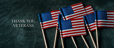 some small flags of the United States and the text thank you veterans on a dark gray surface, in a panoramic format to use as web banner or headerの写真素材