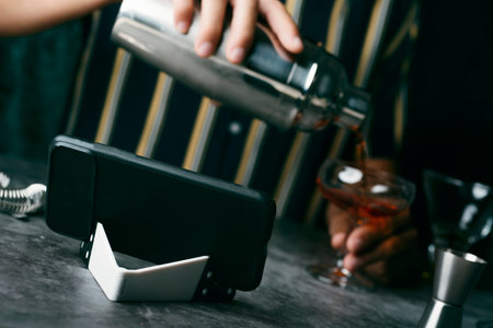 a young caucasian man, wearing a striped shirt, is preparing a cocktail in a metal shaker, following...