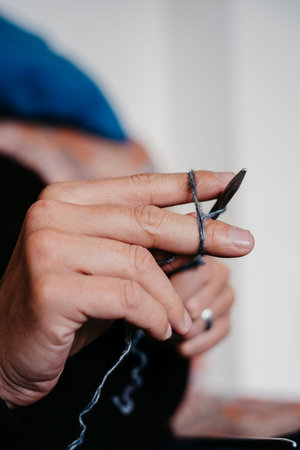closeup o a caucasian man knitting a piece with a gray yarn, sitting on a couch