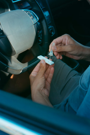 a young man, in spring or summer casual wear, places his own sample into the covid-19 antigen diagnostic test device while is sitting in the driver seat of his carの写真素材