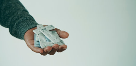 a young man, wearing a gray sweater, has a bunch of covid-19 antigen diagnostic test devices in his hand, in a panoramic format to use as web banner or header, and some blank space on the rightの写真素材