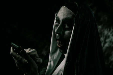 closeup of a scary evil nun, with bloody teeth, in a typical black and white habit, using her smartphoneの写真素材