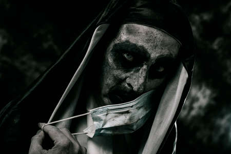 a scary evil nun, in a black and white habit, covers her mouth with a dirty disposable face maskの写真素材