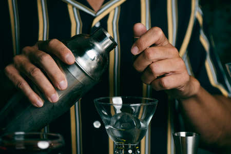 a young caucasian man indoors, wearing a striped shirt, prepares a cocktail in a metal shakerの写真素材