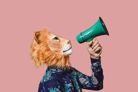 a young man wearing a lion mask speaks into a green megaphone, against a pink backgroundの写真素材