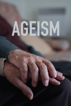 the word ageism and a senior caucasian man and a senior caucasian woman holding hands with affection, sitting in a couchの写真素材