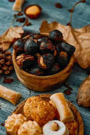 closeup of a plate with some different confections eaten in Spain on All Saints Day, such as assorted Panellets or Huesos de Santo, on a table next to a bowl with some roasted chestnutsの写真素材
