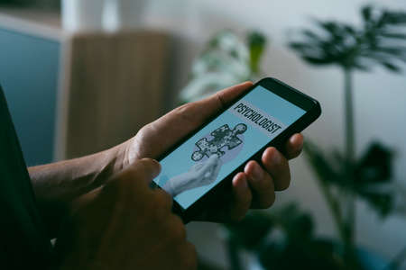 a young caucasian man, at his home, looks for a psychologist online with his smartphone, with a simulated search engine in its screen that reads psychologistの写真素材