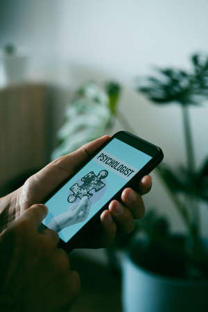 closeup of a young caucasian man, at home, searching a psychologist online with his smartphone, with a simulated search engine in its screen that reads psychologistの写真素材