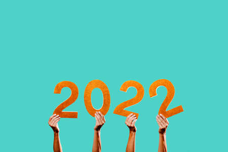 men hands holding some golden three-dimensional numbers forming the number 2022, as the new year, on a blue background with some blank space on topの写真素材