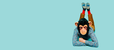 man wearing a monkey mask is looking ahead while is lying face down on a blue background with some...