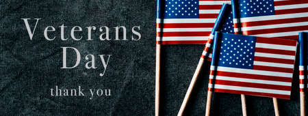 the text Veterans Day, thank you, and some small flags of the United States on a dark gray surface, in a panoramic format to use as web banner or headerの写真素材