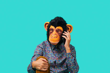 closeup of a young man wearing a monkey mask talking on the phone on a blue backgroundの写真素材