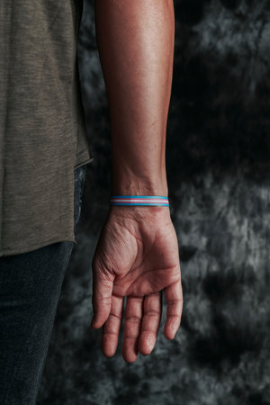 closeup of a young person, seen from behind, wearing a wristband patterned with a transgender pride...