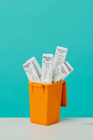 closeup of some used covid-19 antigen diagnostic test devices in a garbage can, on a white surface, against a blue backgroundの写真素材