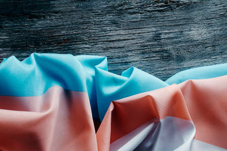 high angle view of a transgender pride flag draped on a rustic gray wooden surface, with some blank space on topの写真素材