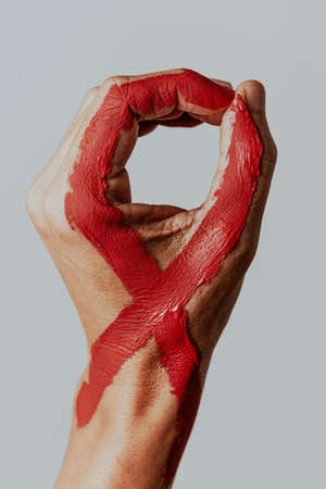 closeup of the hand of a man with a red awareness ribbon for the fight against AIDS painted in it, against an off-white backgroundの写真素材