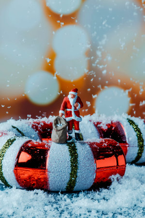 a miniature santa carrying a sack with gifts on a fake candy cane and some fake snow falling on him