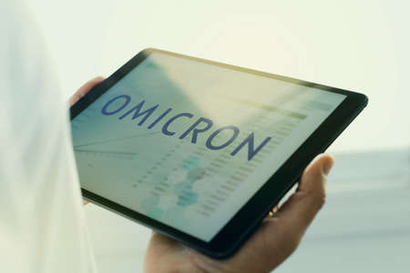 closeup of a doctor man, wearing a white coat, having a digital tablet in his hands with the text omicron in its screen, for the SARS-CoV-2 Omicron variantの写真素材