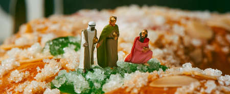 the three kings, melchior, caspar and balthazar, on top of a roscon de reyes, the spanish three kings cake eaten on epiphany day, in a panoramic format to use as web banner or headerの写真素材