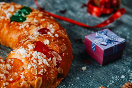 closeup of a spanish roscon de reyes, the typical king cake eaten traditionally on epiphany day, on a gray rustic table, next to a giftの写真素材