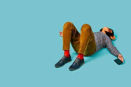 a fun man, wearing a monkey mask, is lying down on a blue background while is holding his smartphone in his hand, and some blank space on the leftの写真素材