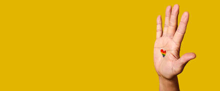 the hand of a man with a heart-shaped rainbow flag painted in his palm on a yellow background with some blank space on the left, and a panoramic format to use as web banner or headerの写真素材