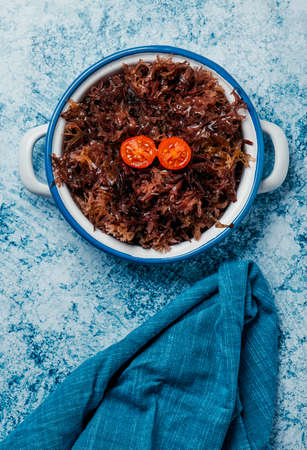 high angle view of a white enamel saucepan with some cooked irish moss, on a bluish stone surface next to a blue napkinの写真素材