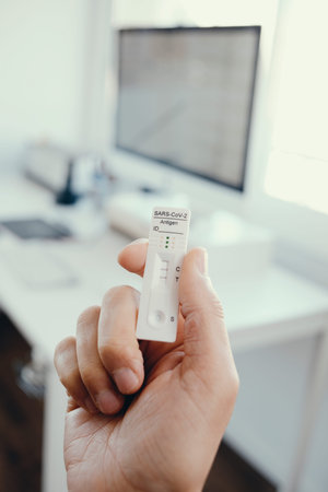 closeup of a young man in the office having in his hand a covid-19 antigen diagnostic test device...