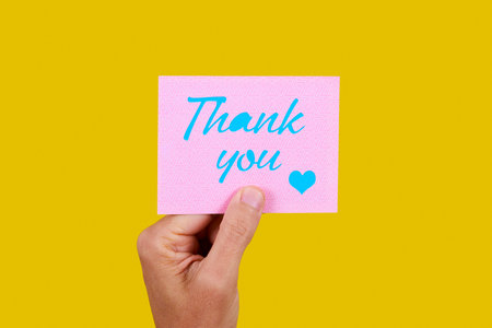closeup of a man with a pink piece of paper with the text thank you written in blue, on a yellow...