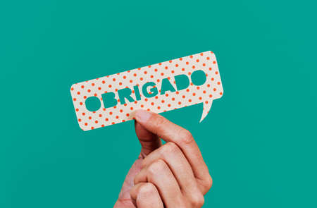 closeup of a man showing a paper speech bubble with the text thank you written in portuguese, on a green backgroundの写真素材