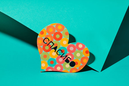 a colorful paper heart with the text thank you written in russian, on a green background