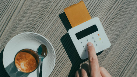 high angle view of a young man, at a table of a sidewalk cafe, inserting the PIN code of his credit...