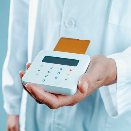 a doctor man, in a white coat, has a wireless payment terminal in his hand with a golden credit card...